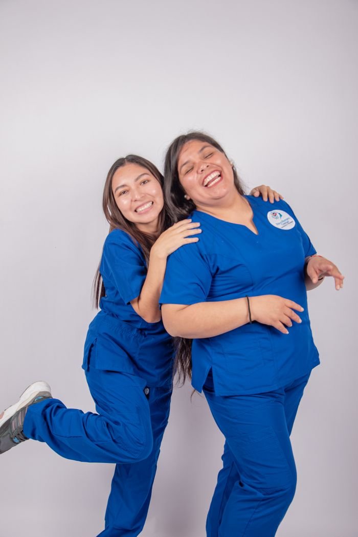 Two smiling nurses in blue uniforms enjoying a joyful moment, showcasing teamwork and positivity.