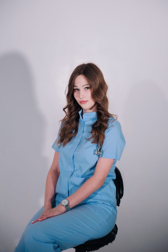 A seated woman in a blue uniform posing against a plain background.